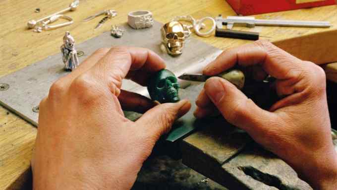 A pair of hands working on a skull-shaped piece of jewel