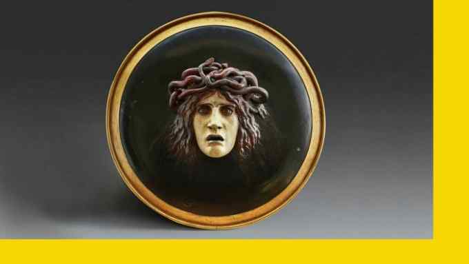 A round black plate with a woman’s head emerging from it, complete with snaky hair