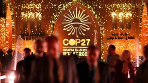 People pass in front of a wall lit with the sign of COP27