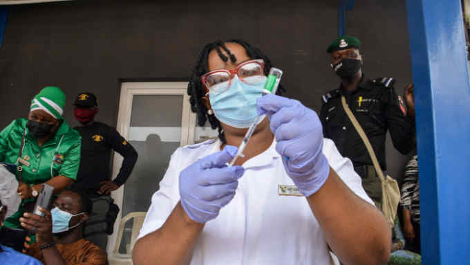 A health care worker prepares to administer a dose of Oxford/AstraZeneca vaccine at a hospital. Behind her are health and military personnel