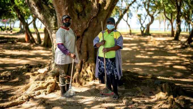 Cleaners wear facemasks, in accordance with Government guidelines, as they pause under a tree while clearing litter in a park in Mauritius