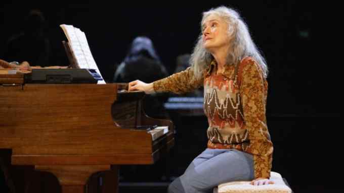 A middle-aged woman sits at a piano, looking wistful
