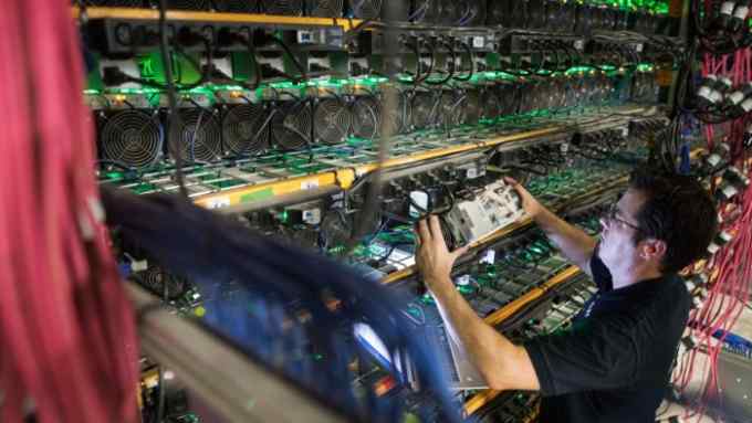 A man removing a computer unit from a wall-mounted bank of units in a cryptocurrency mining facility