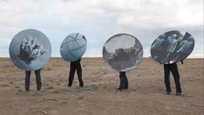 Four people holding large circles printed with black and white photos above their faces