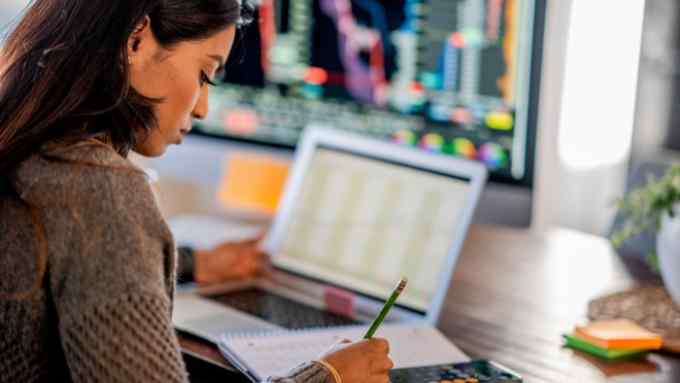 A woman tracking and trading stocks using laptop and desktop computer