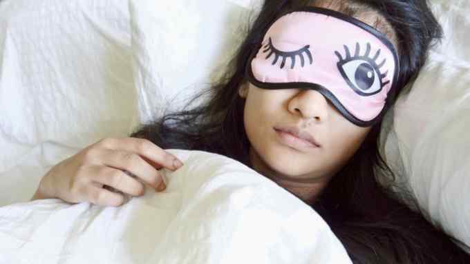 A woman lies in bed wearing a sleep mask