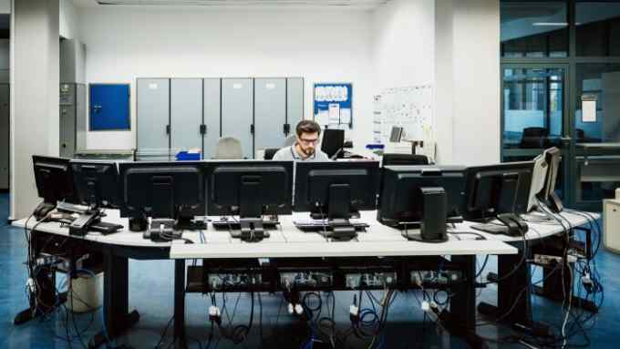 A person sitting down, working behind a desk filled with desktop computers