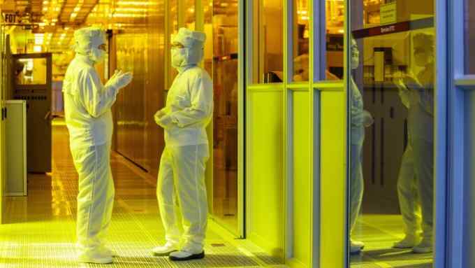 Two workers in protective clothing talking inside a chip-manufacturing plant