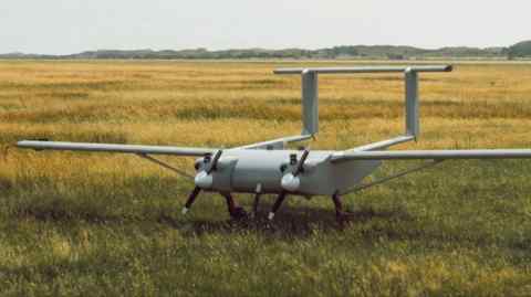 A flying vehicle with propellers, wings and tail fins in a field