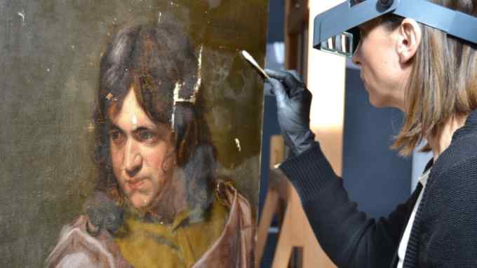 A woman wearing goggles and gloves uses a cotton bud to dab a painting of a young man whose canvas is scratched