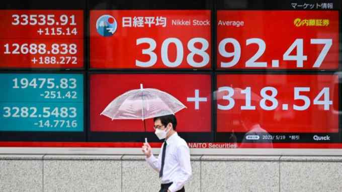 A man walks past an electronic board showing the numbers on the Tokyo Stock Exchange along a street in Tokyo