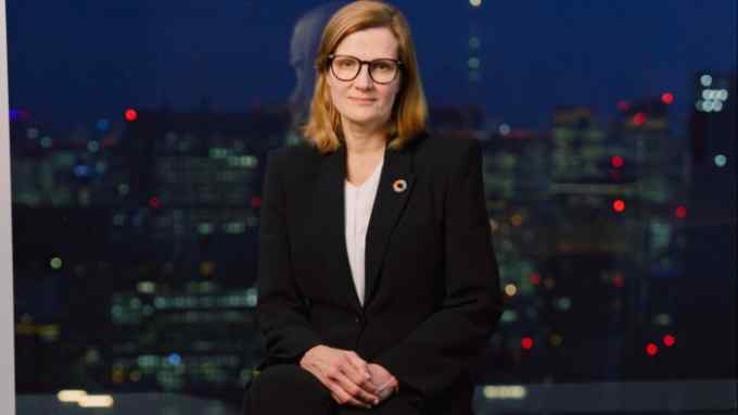 A woman with glasses, with a night-time city skyline behind her