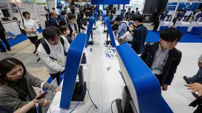 Visitors look at screens displaying Japanese company Tomorrow Net’s navigation-type AI communication tool “CAT.AI” with a ChatGPT function
