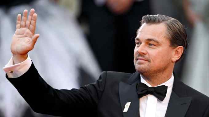 Actor Leonardo DiCaprio in a formal suit waving to the crowd