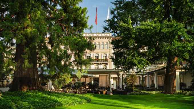 Large trees on a lawn in front of the neoclassical facade of Zürich’s Baur au Lac hotel