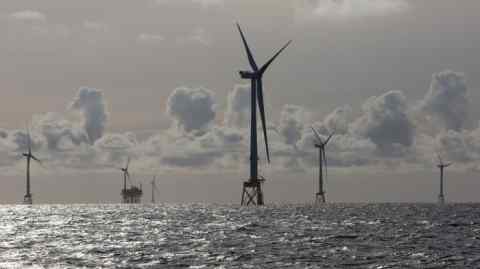View of silhouetted wind turbines in the distance with sparkling sea in the foreground