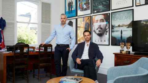 Two men in an office in front of a wall of film posters