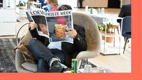 A man sits in a chair reading a magazine with pretzels on its cover