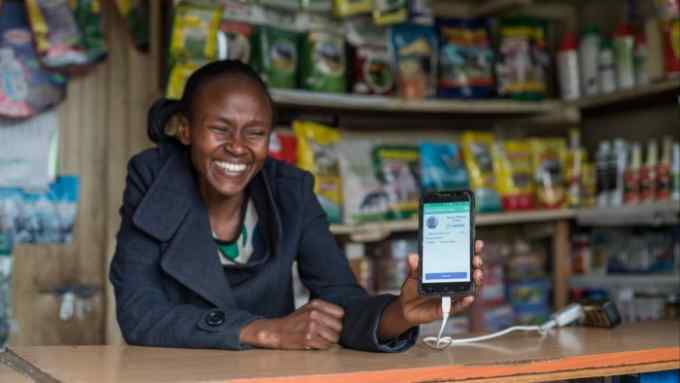 A Kenyan woman holds a phone displaying the Apollo Agriculture app