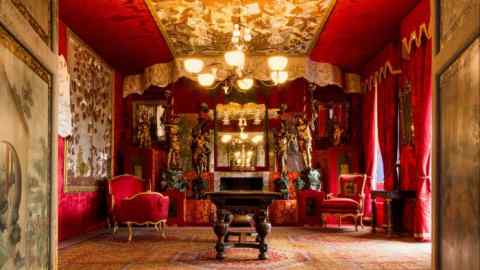 A room decorated with carpeted floor, velvet seats, wooden tables, silk curtains and ornate chandelier