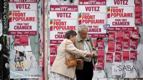 A man and a woman standing in front of election posters of the New Popular Front on a wall in Paris