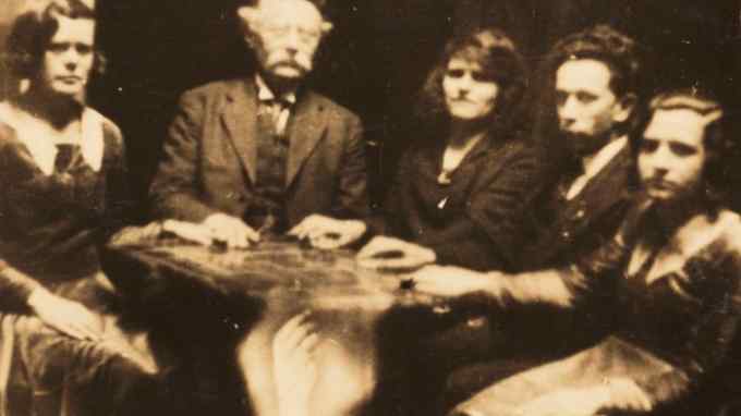 A photograph of a seance c1920 taken by spiritualist William Hope. Hope used double exposure to superimpose an image of a ghostly arm on the table stand. His deceptions were uncovered by a private investigator in 1922