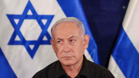 Close up of a pensive looking Benjamin Netanyahu in front of a flag of Israel
