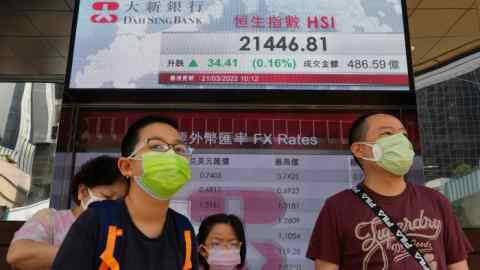 People walk past a bank’s electronic board showing the Hong Kong share index at Hong Kong Stock Exchange