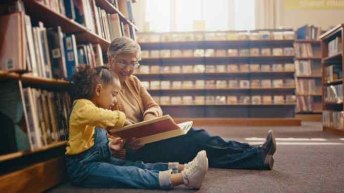 Grandmother with grandchild sitting on the floor of a library with a book for reading