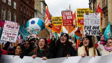 Young teachers marching holding up placards and banners in favour of strike action