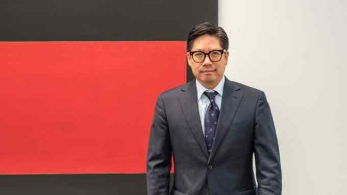 A man in a blue suit with glasses looks intent in front of a black and red painting