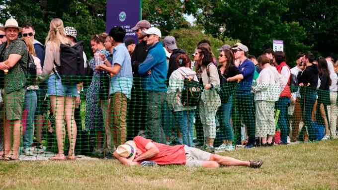 People in the queue for Wimbledon in Wimbledon Park, with a man lying asleep on the grass beside them