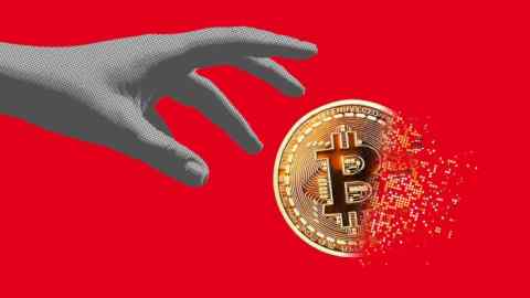 A hand reaches for a fragmenting bitcoin against a red background
