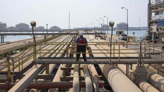 An employee looks out across oil pipes used for landing and unloading crude and refined oil at the North Pier Terminal, operated by Saudi Aramco, in Ras Tanura, Saudi Arabia