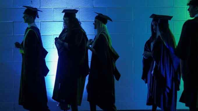 A line of graduates in mortar boards and gowns attend a ceremony