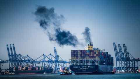 Black smoke emanates from a container ship leaving port