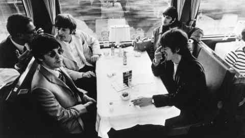 Four well-dressed men in the 1960s sit around a table in the carriage of a train