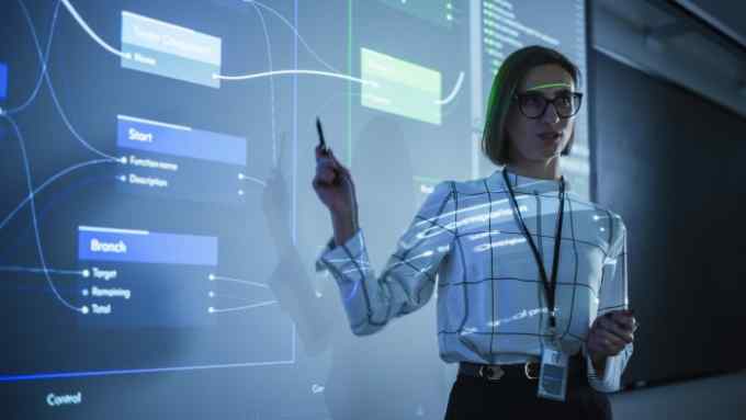 Portrait of a Young Female Professor Explaining Big Data and Artificial Intelligence Research Project in a Dark Room with a Screen Showing a Neural Network Model