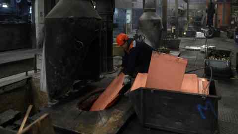 A worker loads copper sheets into a furnace in a foundry