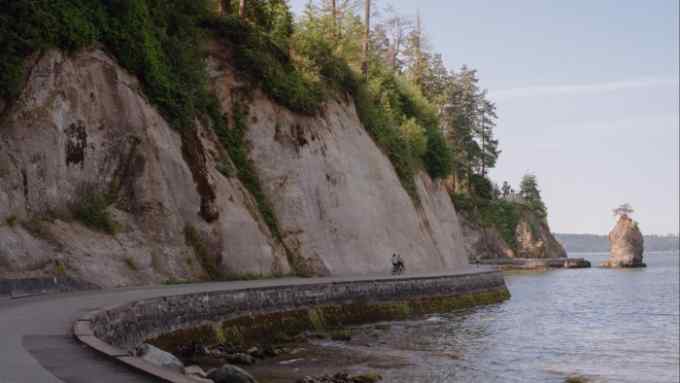 Cliffs with trees at the top to the left of the Stanley Park Seawall; the sea is to the right