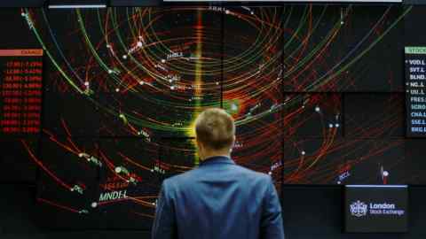 An employee views a FTSE 100 share index board in the atrium of the London Stock Exchange Group