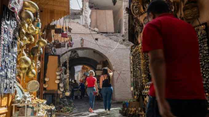 Tourists walk under a building marked with a red ‘X,’ symbolizing it is unsafe after an earthquake