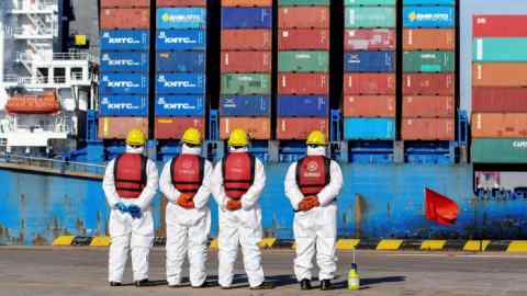 Employees wearing personal protective equipment look on by a cargo ship at a port in Qingdao in China