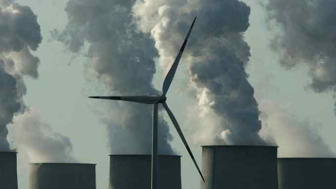 A loan wind turbine spins as exhaust plumes from cooling towers at the Jaenschwalde lignite coal-fired power station