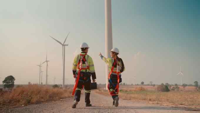 Asian man and female engineer walking side by side to where there are several wind turbines