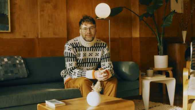 A sweater-clad Broughton sits on a sofa at home in north-west London