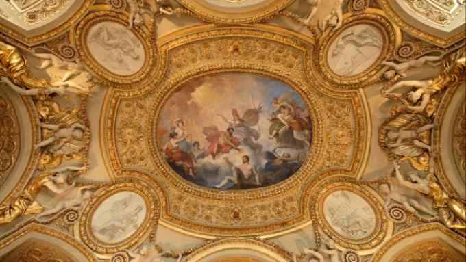 A plaster ceiling covered in gilded mouldings around an oval baroque mythological painting