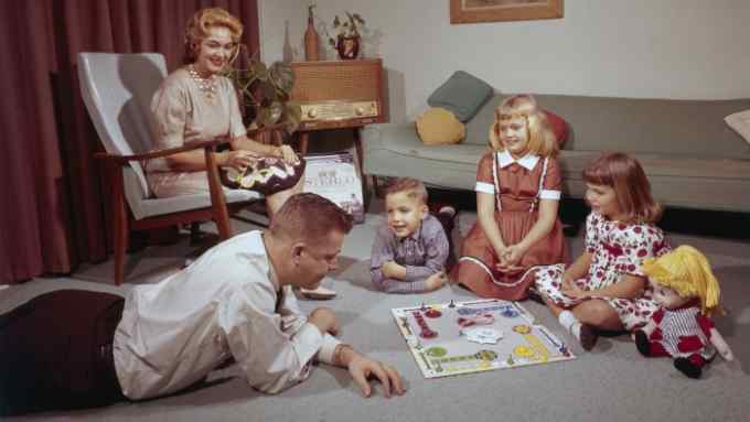 a young family on the floor playing a board game while mum crochets in a chair, 1962