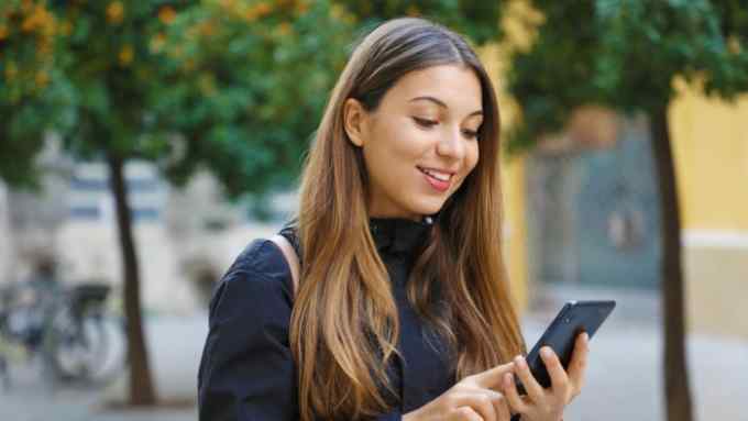 A woman in a street smiles as she looks at a mobile phone screen