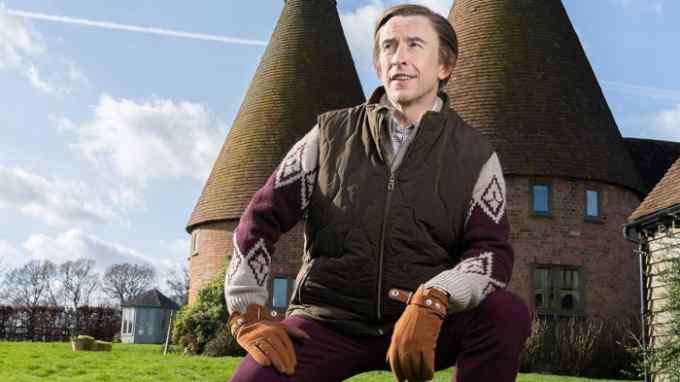 A man in a gilet crouches smugly outside an oast house